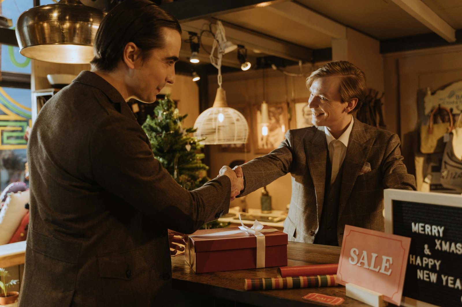 Hem 12 Två män i kostym skakar hand över en butiksdisk vid en "Sale"-skylt, vilket illustrerar den typ av kundservice som leder till positiva kundrecensioner.